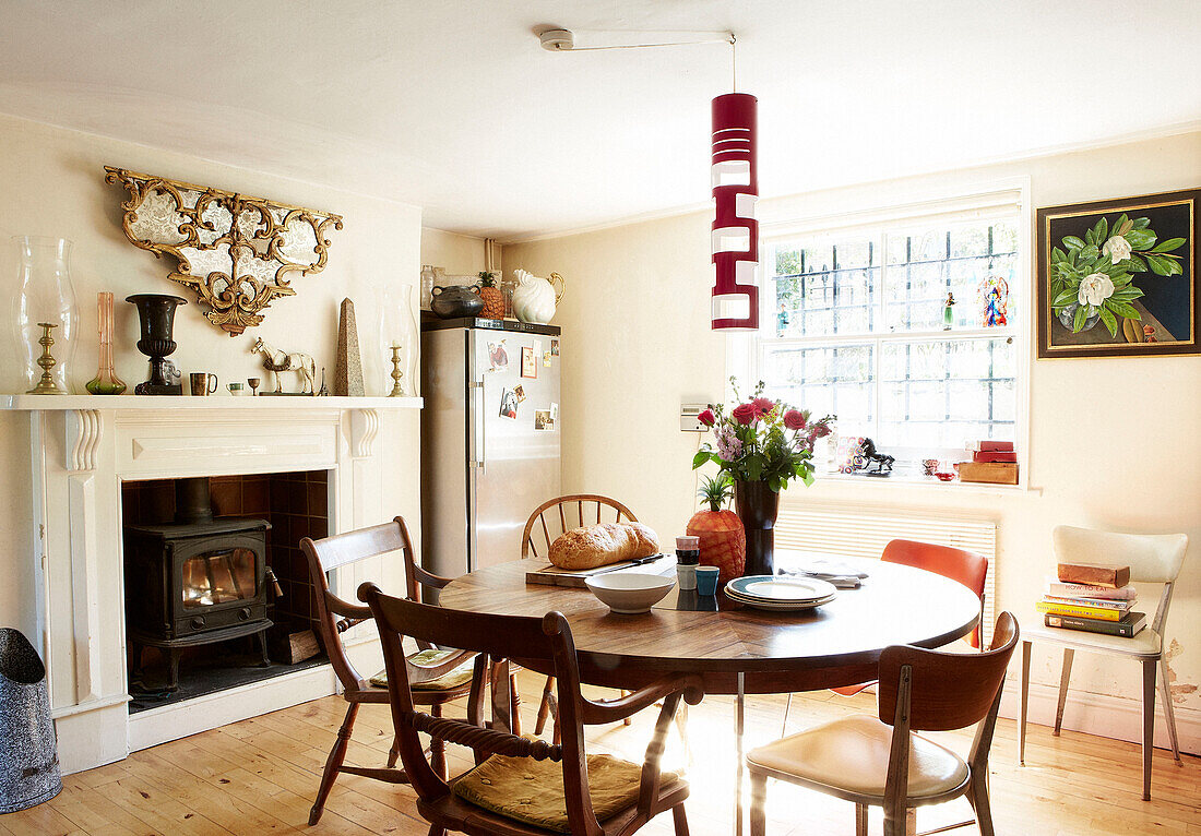 Wooden table and chairs below retro lampshade with lit woodburning stove in London townhouse England UK