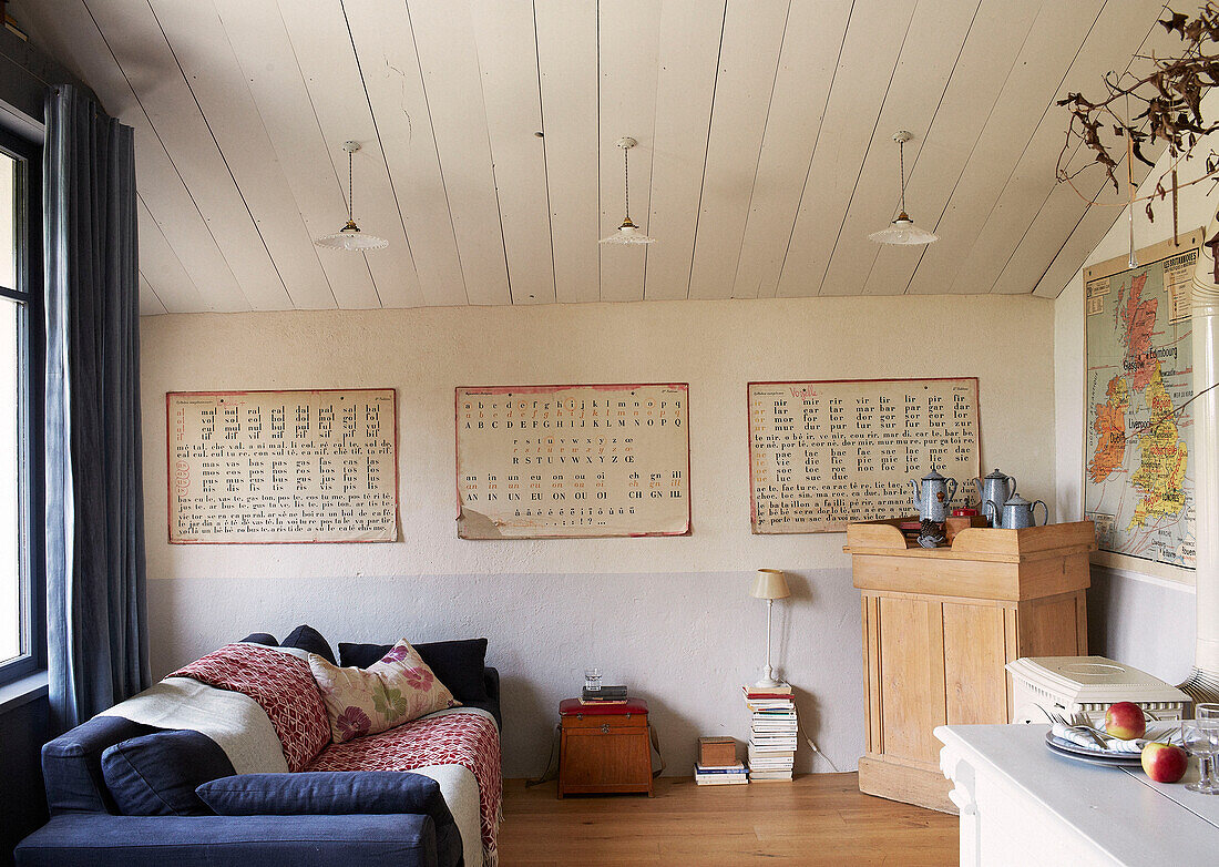 Französischer Text mit blauem Sofa und Wandkarte im Wohnzimmer eines umgebauten Schulhauses in der Bretagne, Frankreich