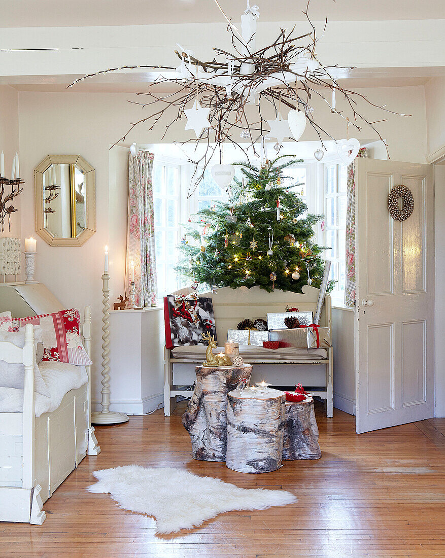 Tagesbett und Holzscheite mit Weihnachtsbaum im Wohnzimmer eines Bauernhauses in Derbyshire England UK