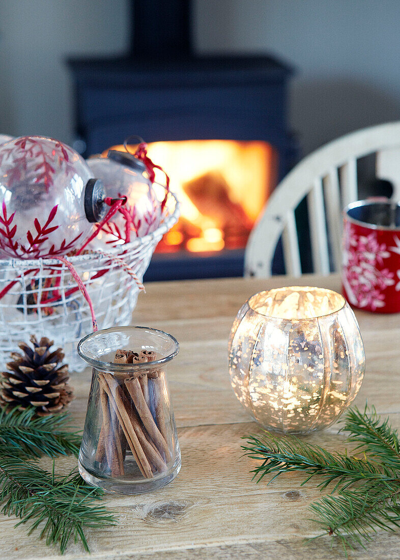 Beleuchtete Kerze mit Zimtstangen und Weihnachtskugeln auf dem Tisch in einem Haus in Devonshire, UK