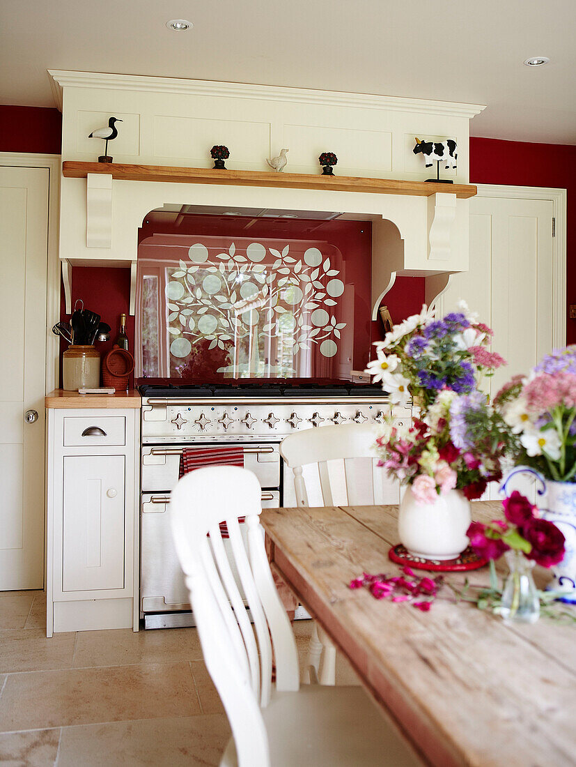Schnittblumen auf einem hölzernen Küchentisch mit rot gemusterter Spritzwand in einem Landhaus in Oxfordshire, England UK