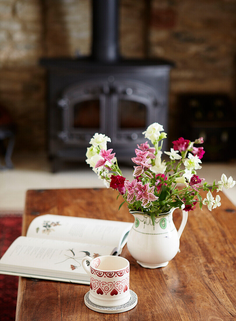 Schnittblumen mit Tasse und aufgeschlagenem Buch auf Holztisch in ländlichem Cottage in Oxfordshire England UK