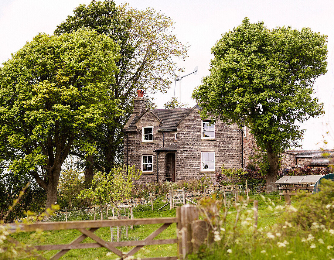 Ländliches Bauernhaus auf einem Grundstück mit Bäumen und Tor in Derbyshire, England, UK
