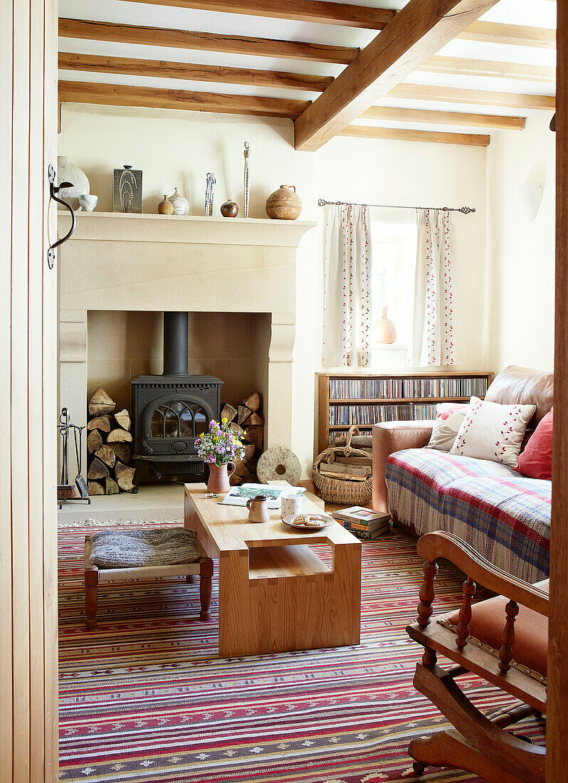 Couchtisch aus Holz auf gestreiftem Teppich mit Holzbrenner im Wohnzimmer eines Bauernhauses in Derbyshire, England, UK