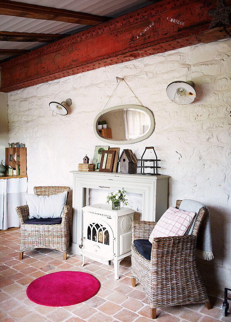 Ovaler Spiegel über einem Kamin mit zwei Korbstühlen in einem bretonischen Bauernhaus, Frankreich