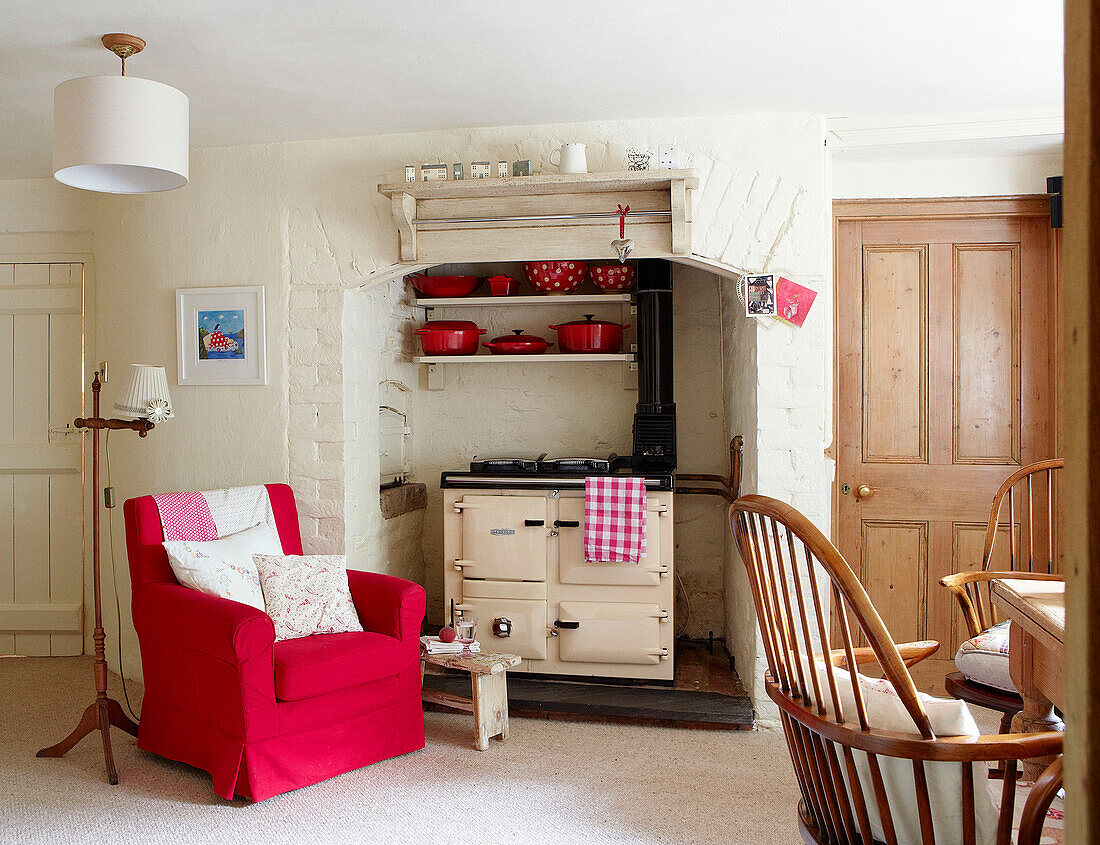 Red armchair beside cream Aga in Devonshire cottage UK