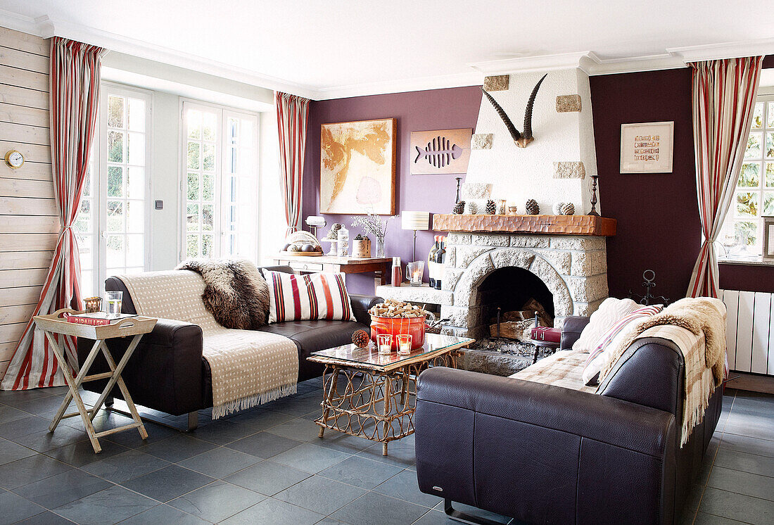 Zwei Sofas in einem lilafarbenen Wohnzimmer mit offenem Steinkamin in einem bretonischen Gästehaus in Frankreich