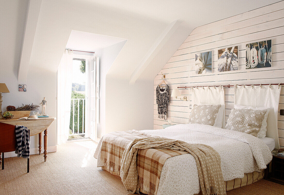 Karierte und getöpferte Decken auf einem Doppelbett in einem sonnenbeschienenen Gästehaus in der Bretagne mit offener Balkontür Frankreich