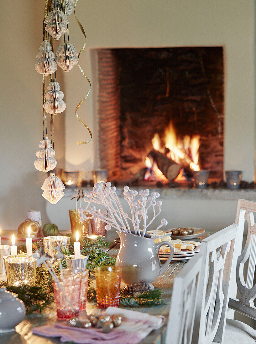 Christmas decorations above dining table by lit fire in Oxfordshire home England UK