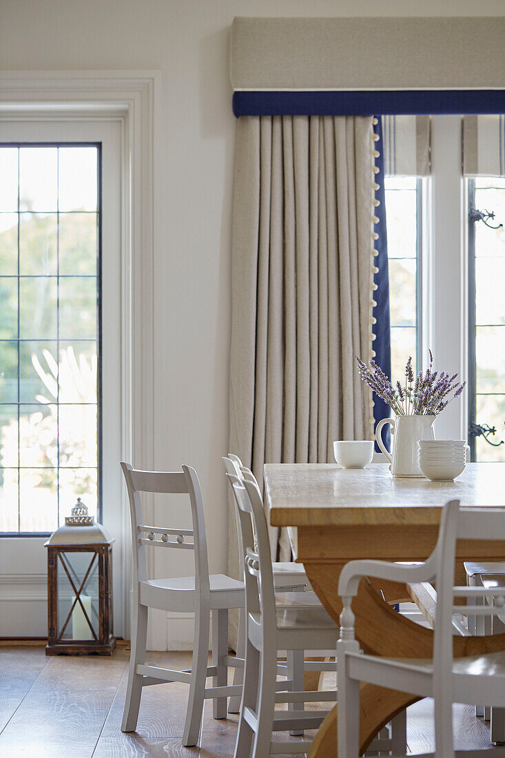 White painted chairs at wooden table in dining room of modernised Northumbrian country house UK