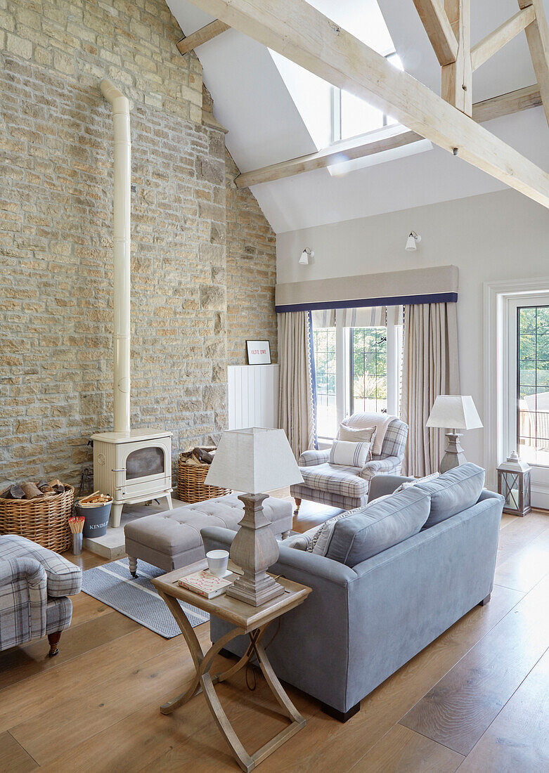 Light blue sofa and cream woodburner in double height living room of modernised Northumbrian country house with exposed stone wall UK