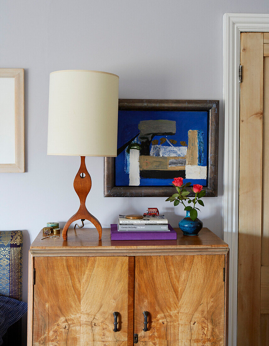 Retro lamp and books with modern artwork on wooden bedside cabinet in Speldhurst home Kent England UK