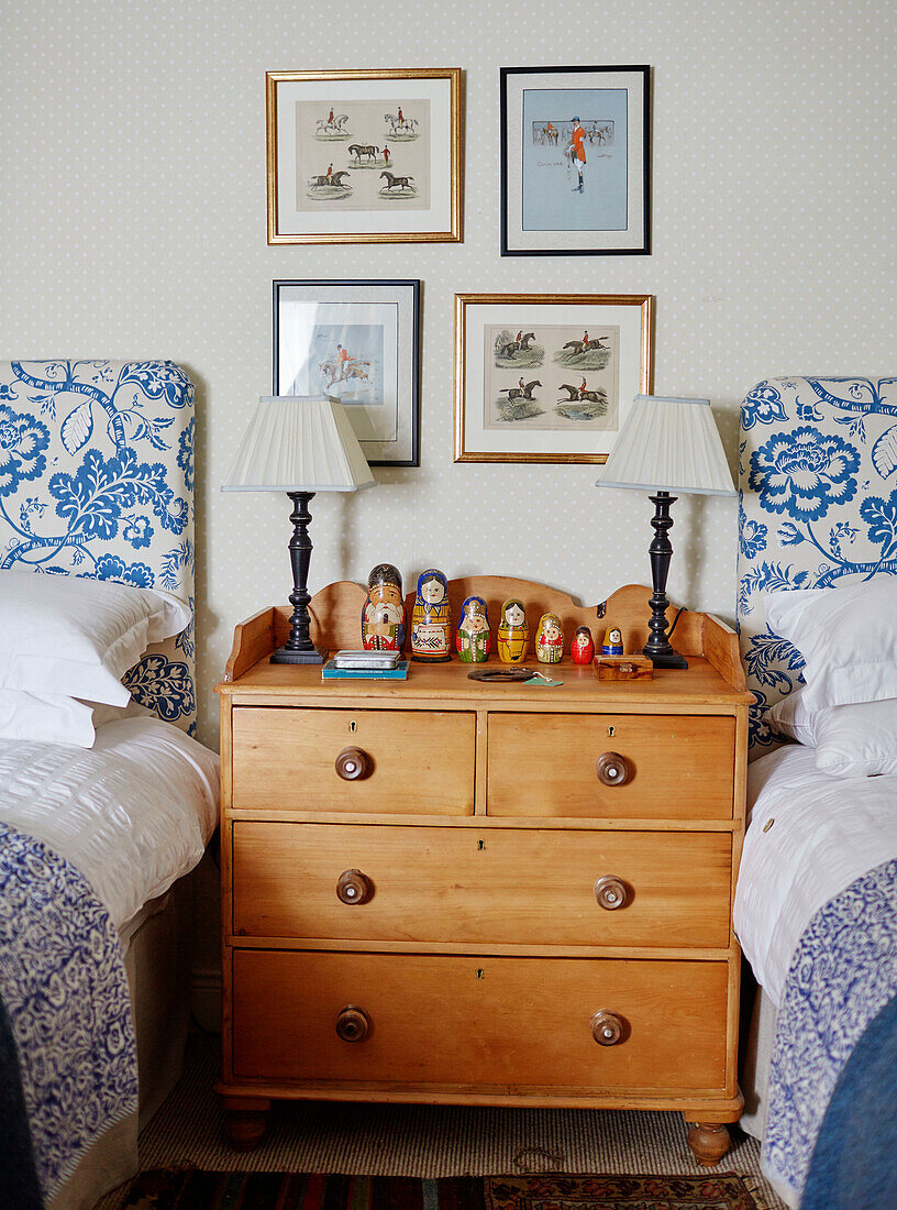 Framed artwork above Russian dolls on wooden chest of drawers with blue floral twin headboards in Hexham home Northumberland UK