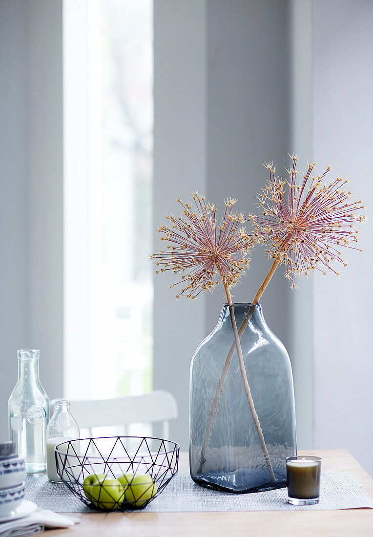 Trockenblumen in einer Vase und Drahtschale mit Äpfeln auf einem Esstisch in einem britischen Studio