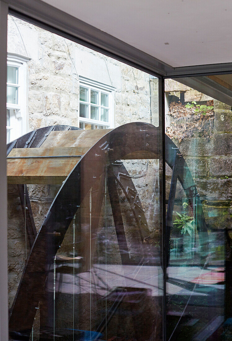 Blick von Anbau durch Glas auf ein Wasserrad in einem renovierten Mühlenhaus aus dem 18. Jahrhundert in Northumbria, UK