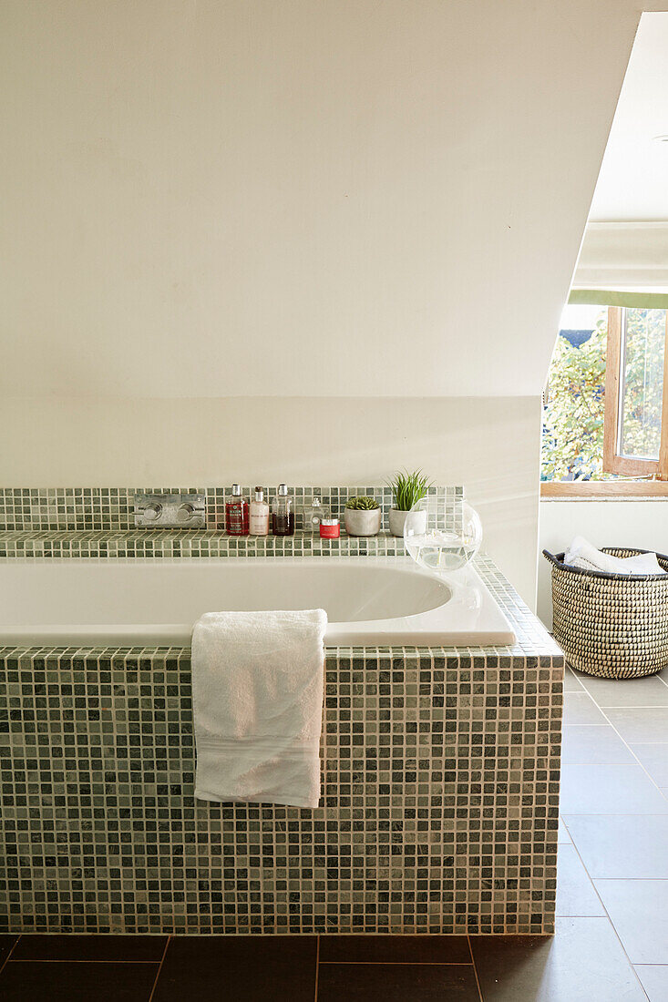Toiletries on green mosaic tiled bath in Kent home, North East England, UK