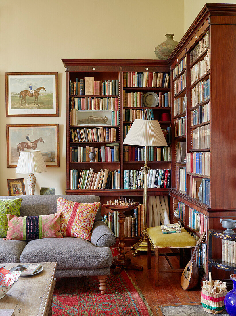 Standard lamps and bookcase with grey sofa in living room Capheaton Hall, Northumberland, UK