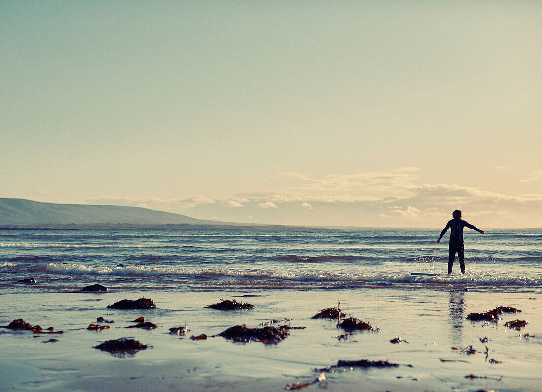 Boy standing at waters edge in wetsuit County Sligo in Connacht, Ireland