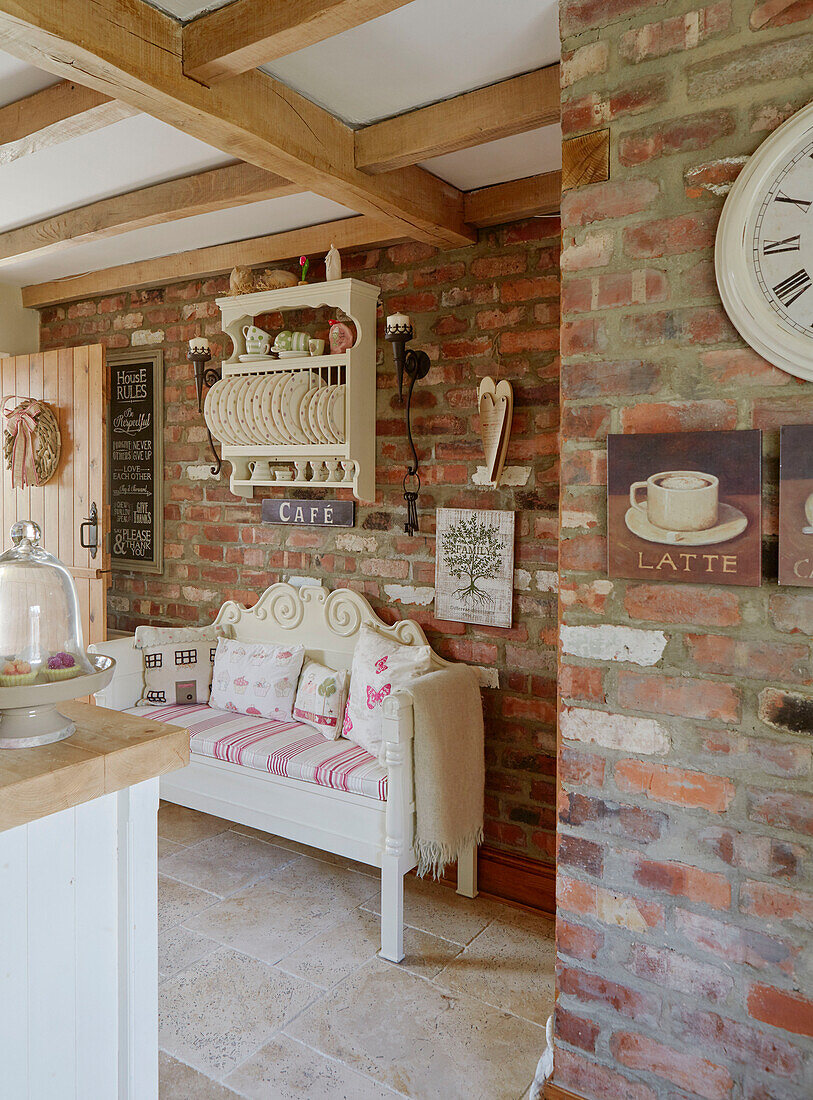 Plate rack above two seater sofa in exposed brick County Durham cottage kitchen, England, UK