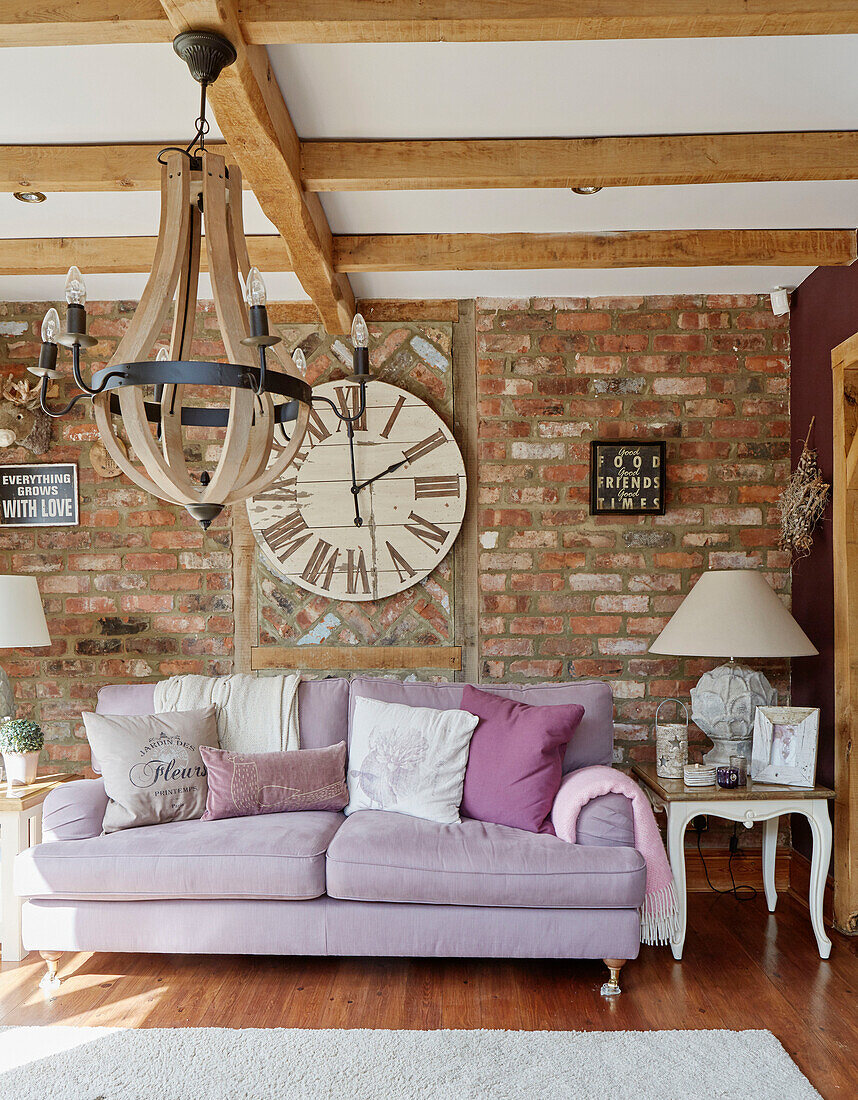 Lilac sofa with large clock in exposed brick living room in County Durham cottage, England, UK