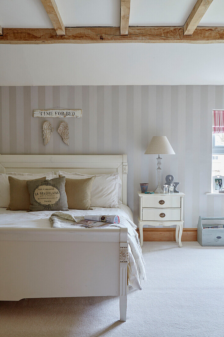Double bed with striped wallpaper below beamed ceiling in County Durham cottage, England, UK