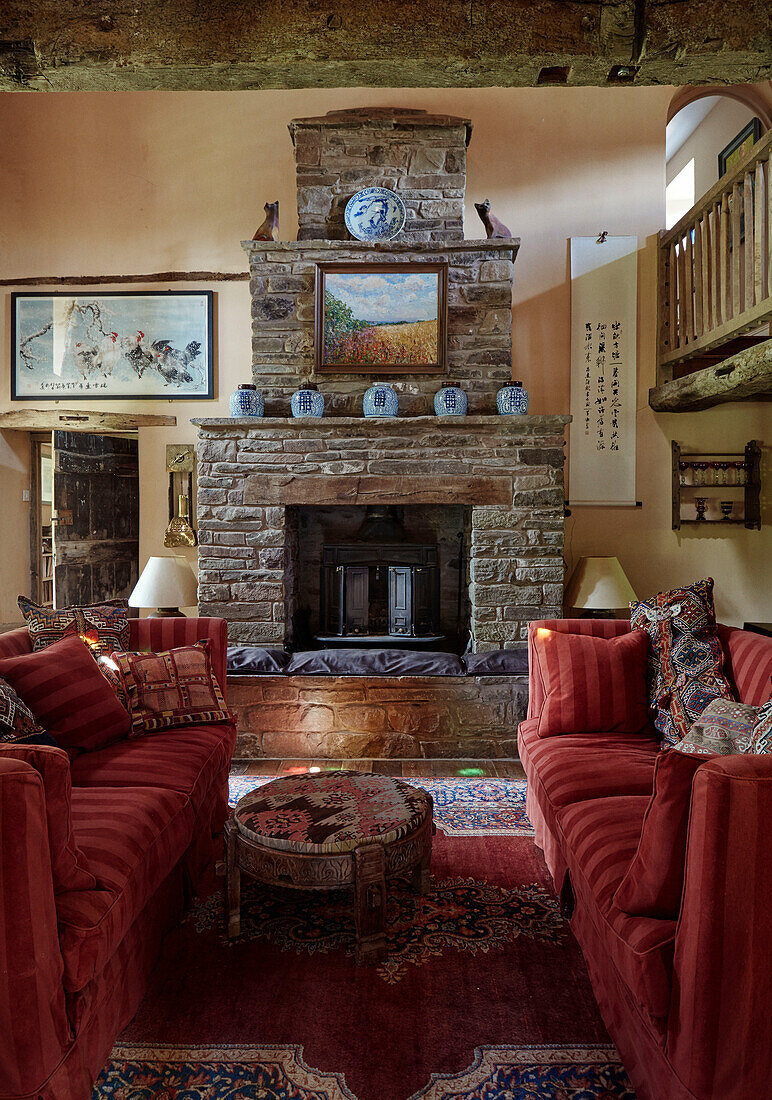 Pair of striped red sofas with exposed stone fireplace in Herefordshire farmhouse, UK