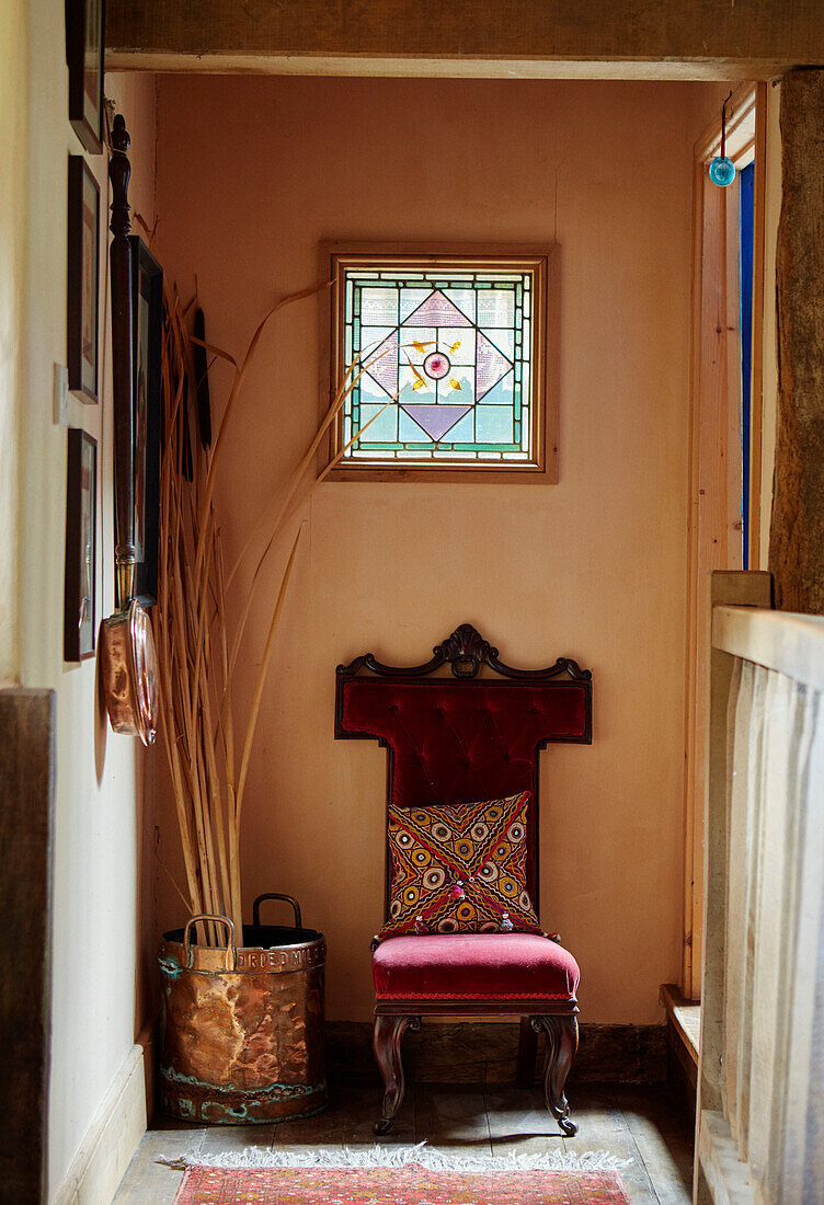 Samtstuhl und Bambushalme unter dem Buntglasfenster in einem Bauernhaus in Herefordshire, UK