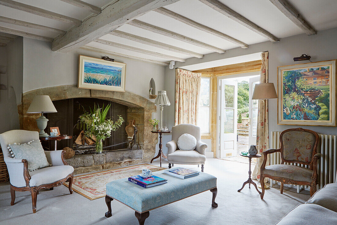 Armchairs and lamps with stone fireplace in living room of Warwickshire farmhouse, UK