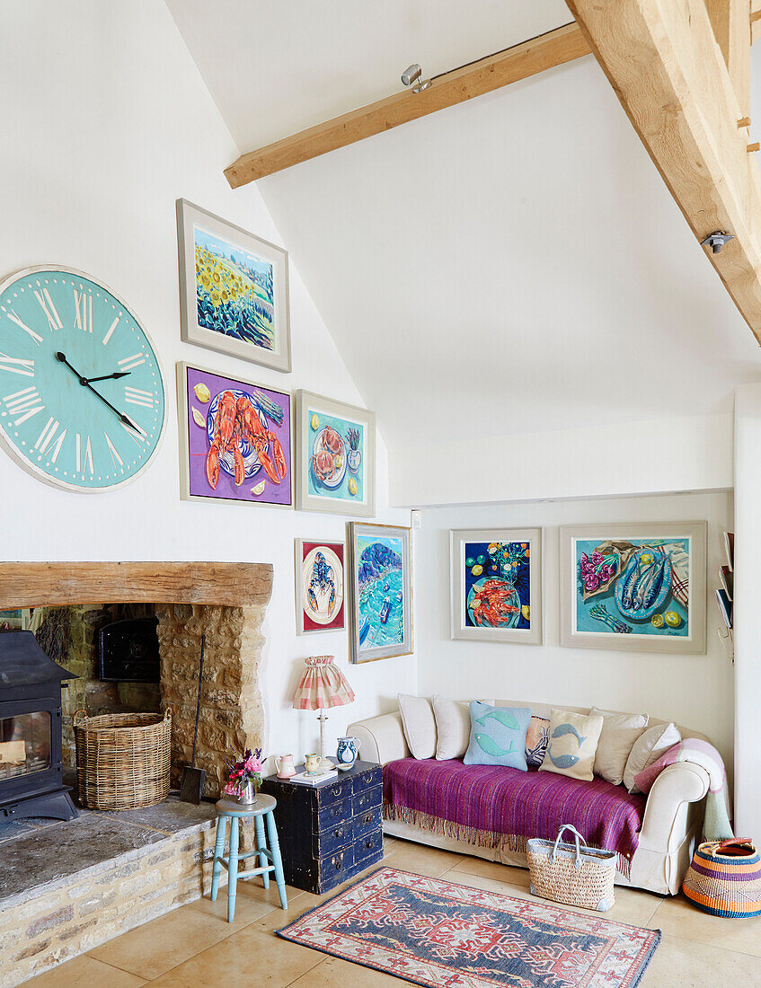 Große Uhr über dem Holzofen mit moderner Kunst in einem Bauernhaus in Warwickshire, UK