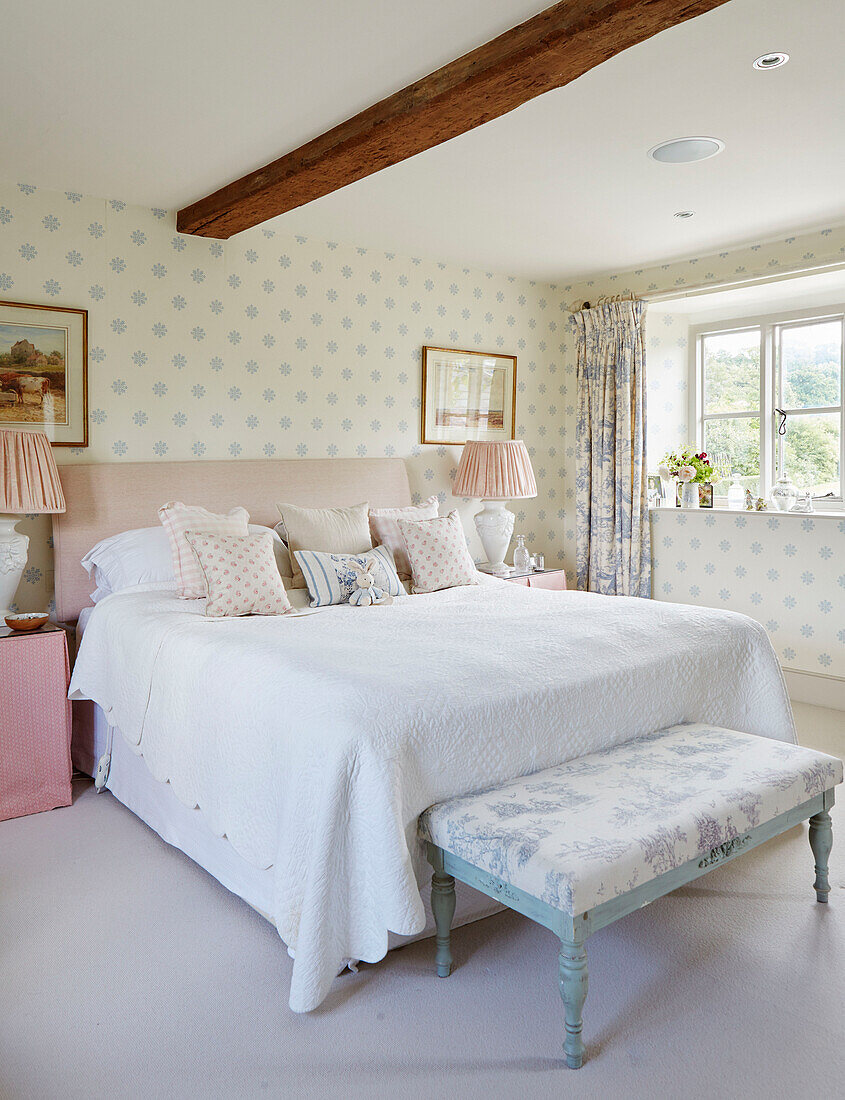 Double bed with floral patterned footstool and lamps in Warwickshire farmhouse, UK