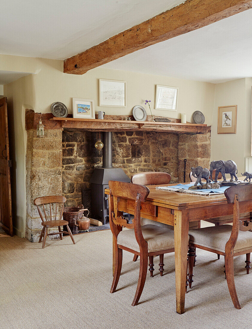 Elephant statues on wooden dining table with exposed stone fireplace in Oxfordshire cottage, UK