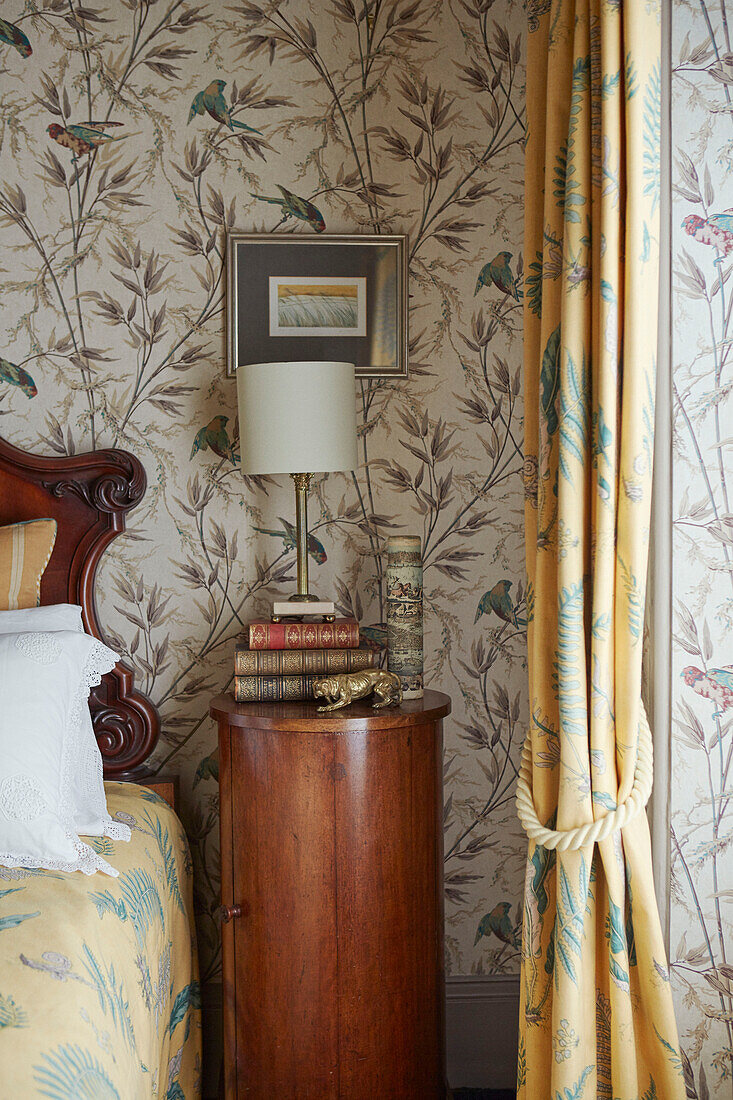 Lamp and books on wooden bedside table with patterned wallpaper in 19th century Georgian townhouse in Talgarth, Mid Wales, UK