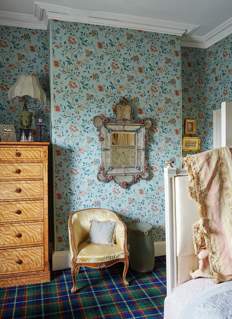 Upholstered chair and tallboy with antique mirror and patterned wallpaper in 19th century Georgian townhouse in Talgarth, Mid Wales, UK