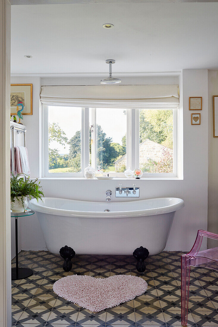 Freestanding bath below window with heartshaped mat and plant stand in Yorkshire home, England, UK