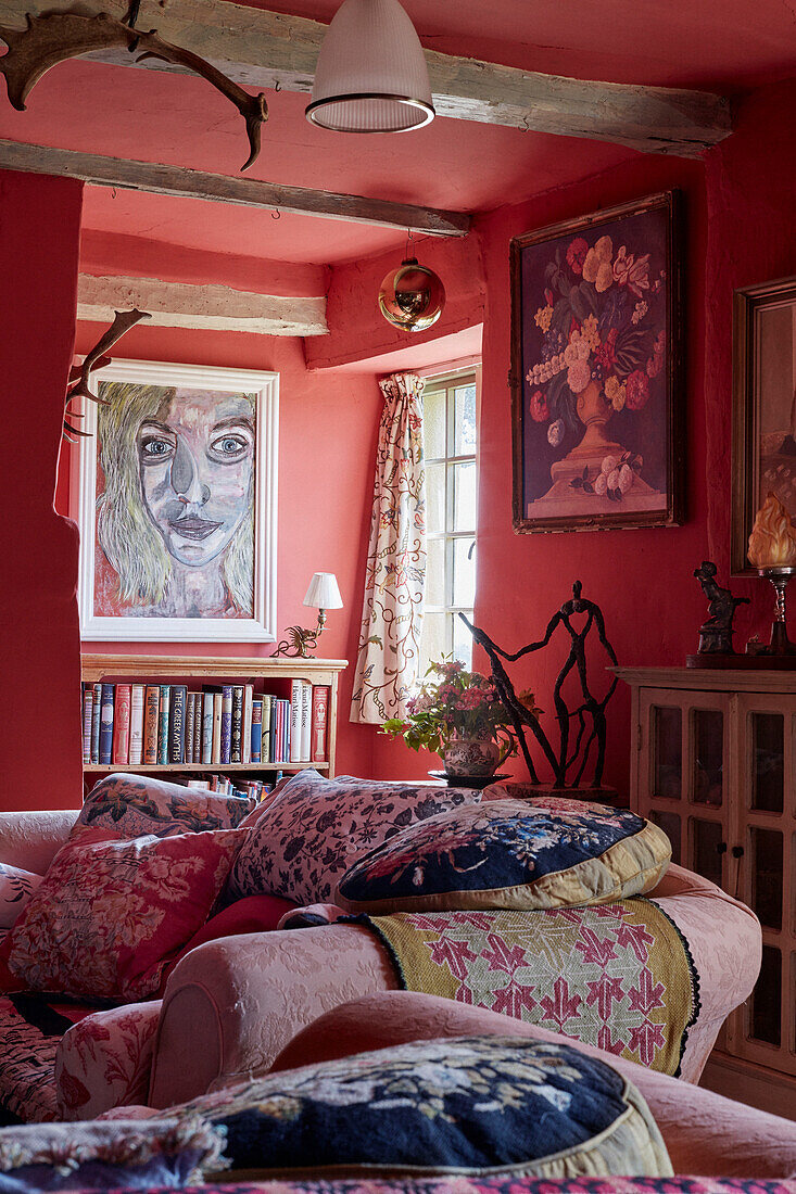 Bücherregal und Kunstwerke mit Blumenkissen auf dem Sofa im Wohnzimmer von einem Cottage in Powys, Wales, UK