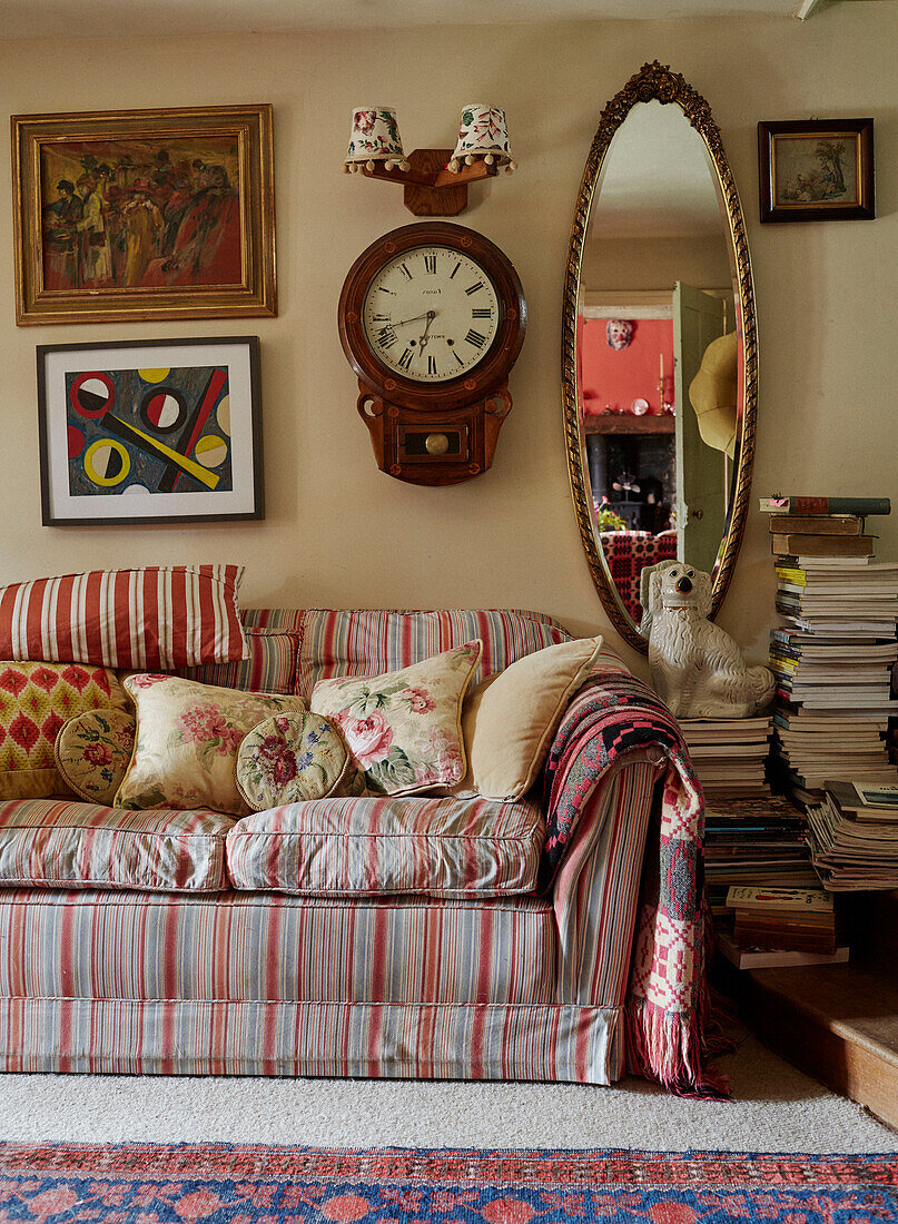 Vergoldeter Spiegel und antike Uhr mit gestreiftem Sofa und Kunstwerken in einem Landhaus in Powys, Wales, UK