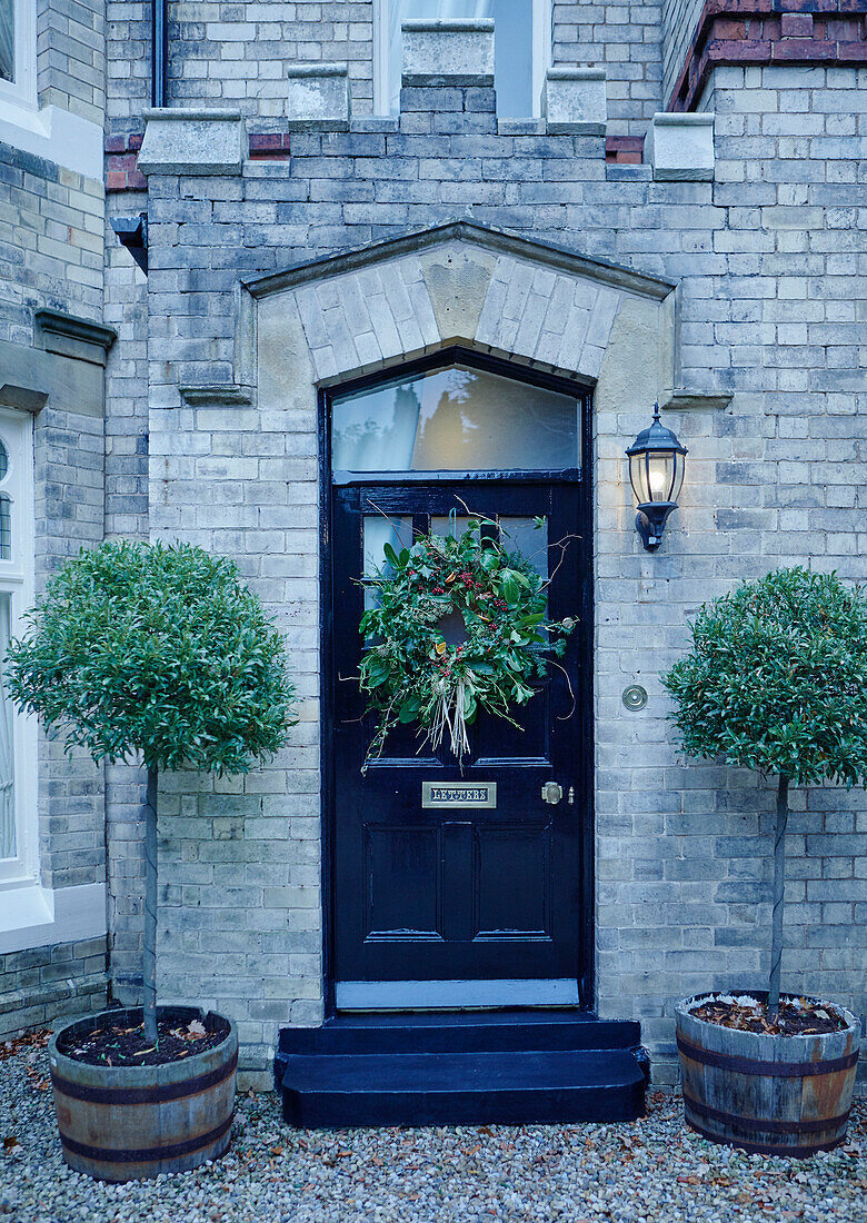 Weihnachtskranz an schwarzer Haustür eines britischen Hauses mit gepflanzten Bäumen