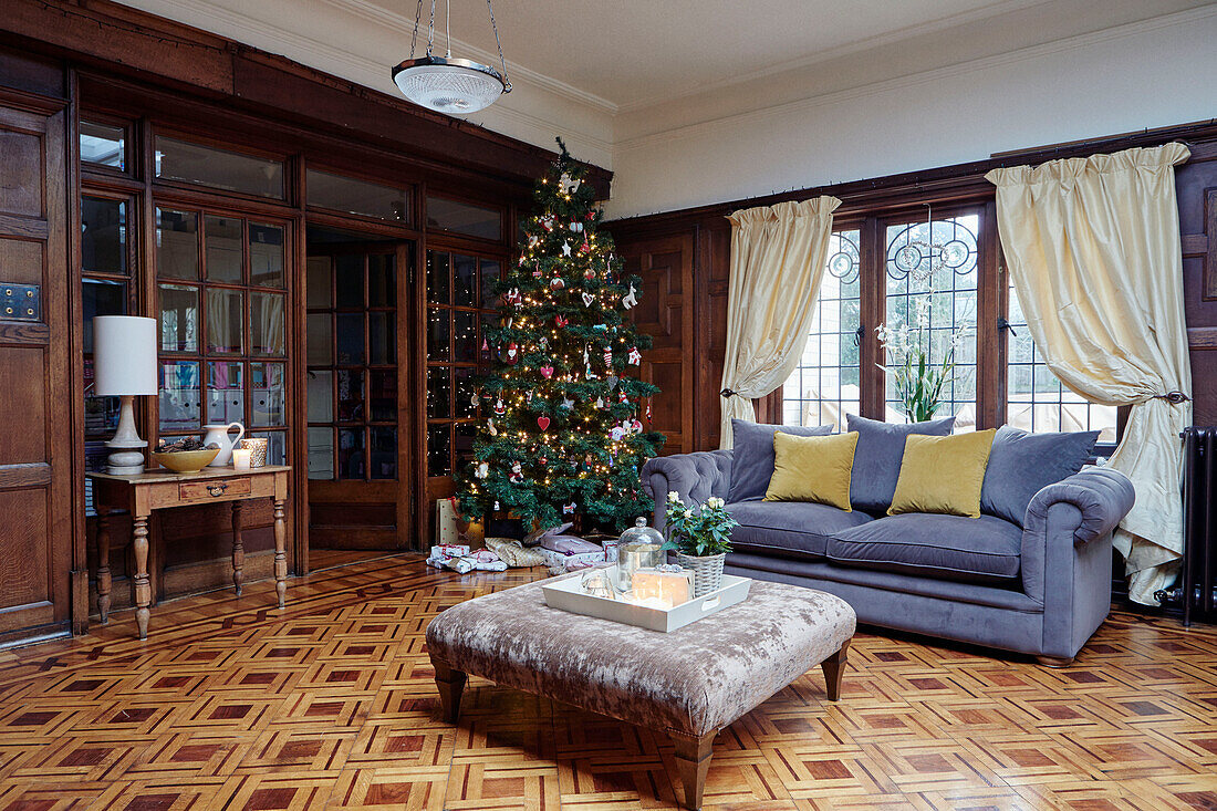 Ottoman and grey velvet Chesterfield with Christmas tree in living room with parquet floor of, UK home