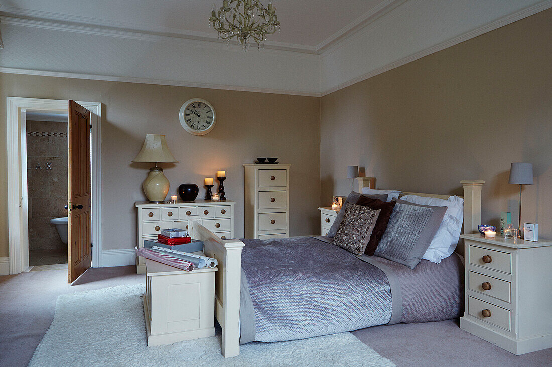 Cremefarbene Stauraummöbel und graues Doppelbett mit offener Tür zum eigenen Bad in einem britischen Haus