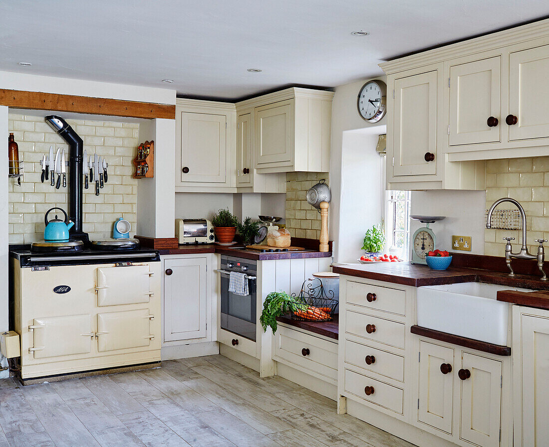 Cream oven and fitted units with butler sink in Sandford St Martin cottage, Oxfordshire, UK
