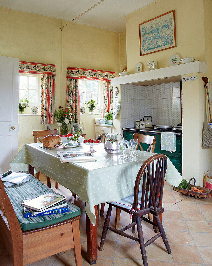 Spotted tablecloth and bench in yellow farmhouse kitchen in Syresham home, Northamptonshire, UK