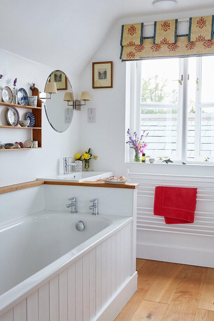 Ornaments on shelf above white tongue and groove bath in Oxfordshire farmhouse, UK