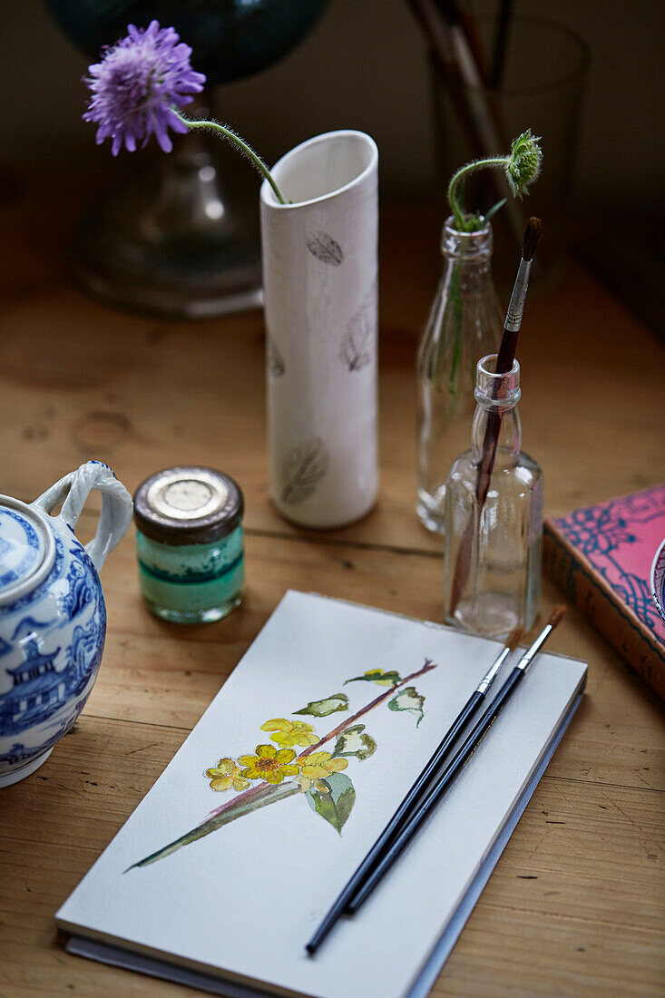 Paintbrushes on art pad with single stem flower in vase Oxfordshire, UK
