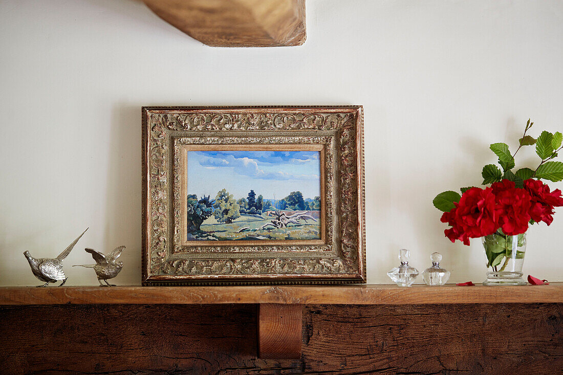 Framed artwork and ornaments with red flowers on wooden mantlepiece in Berkshire cottage, England, UK