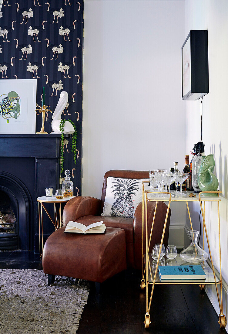 Brown leather armchair and footstool with dark wallpaper at fireside in Victorian semi-detached house South East London, UK