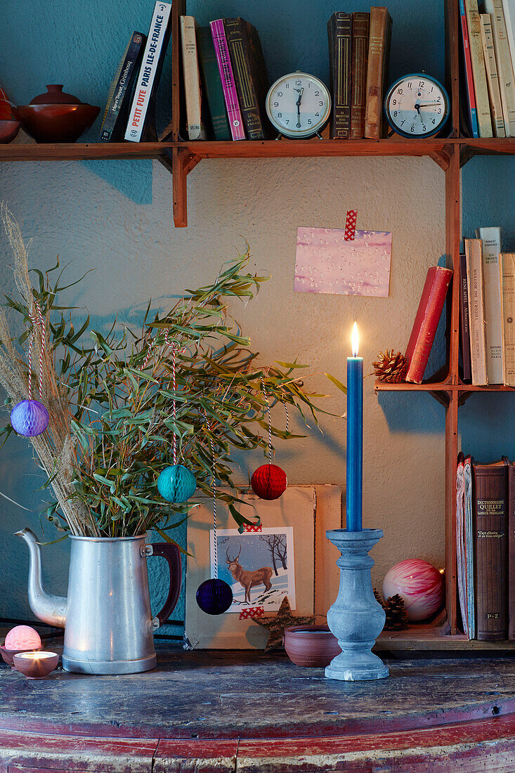 Leaves and lit candle with books on shelves in Brittany cottage, France