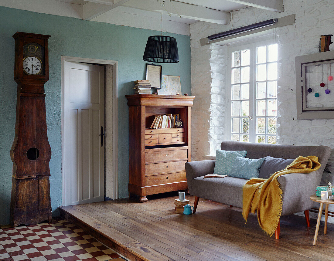 Grey sofa in split level interior of Brittany cottage with old grandfather clock, France
