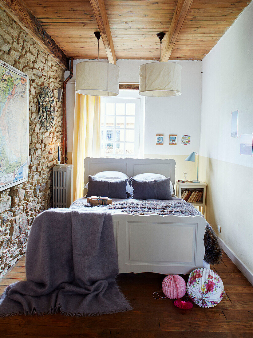 Papierschirme über einem Doppelbett mit freiliegender Steinwand in einem bretonischen Landhaus in Frankreich