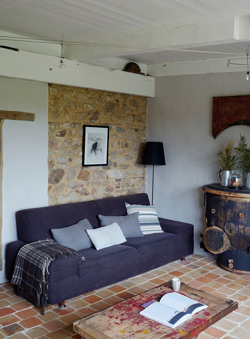 Faltbare Decke auf lilafarbenem Sofa mit freiliegender Steinwand in einem bretonischen Landhaus in Frankreich