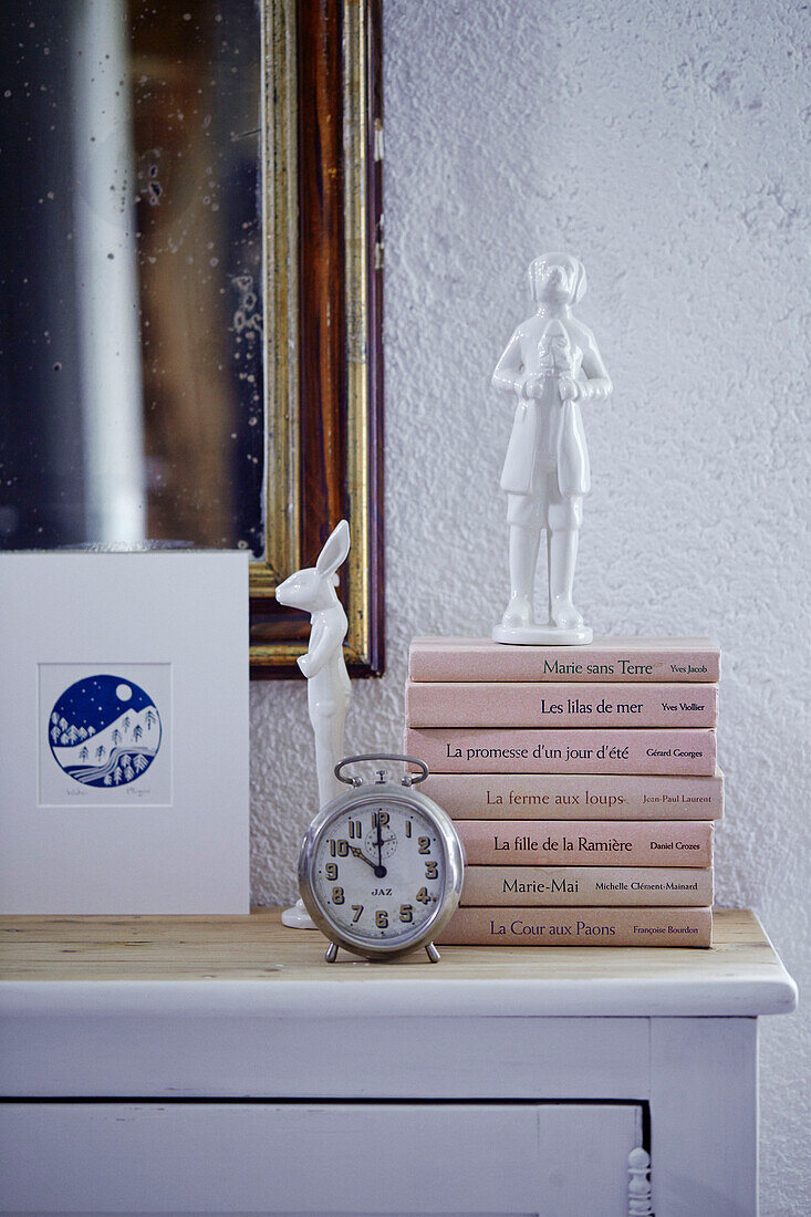 Weiße Ornamente und Wecker mit Büchern auf Anrichte in bretonischem Landhaus in Frankreich
